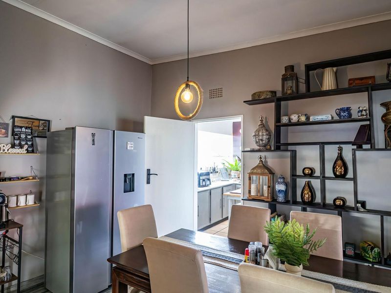 A dining area featuring a modern pendant light and a large built-in wall shelving unit, with a direct view into the adjacent kitchen.