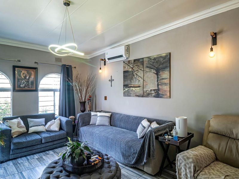 A comfortable living room featuring arched windows, crown molding, tiled flooring, and a wall-mounted air conditioning unit.