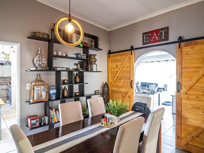Dining room featuring built-in shelving, rustic sliding barn doors, and an arched entryway leading to an adjacent workspace, with tiled flooring throughout.