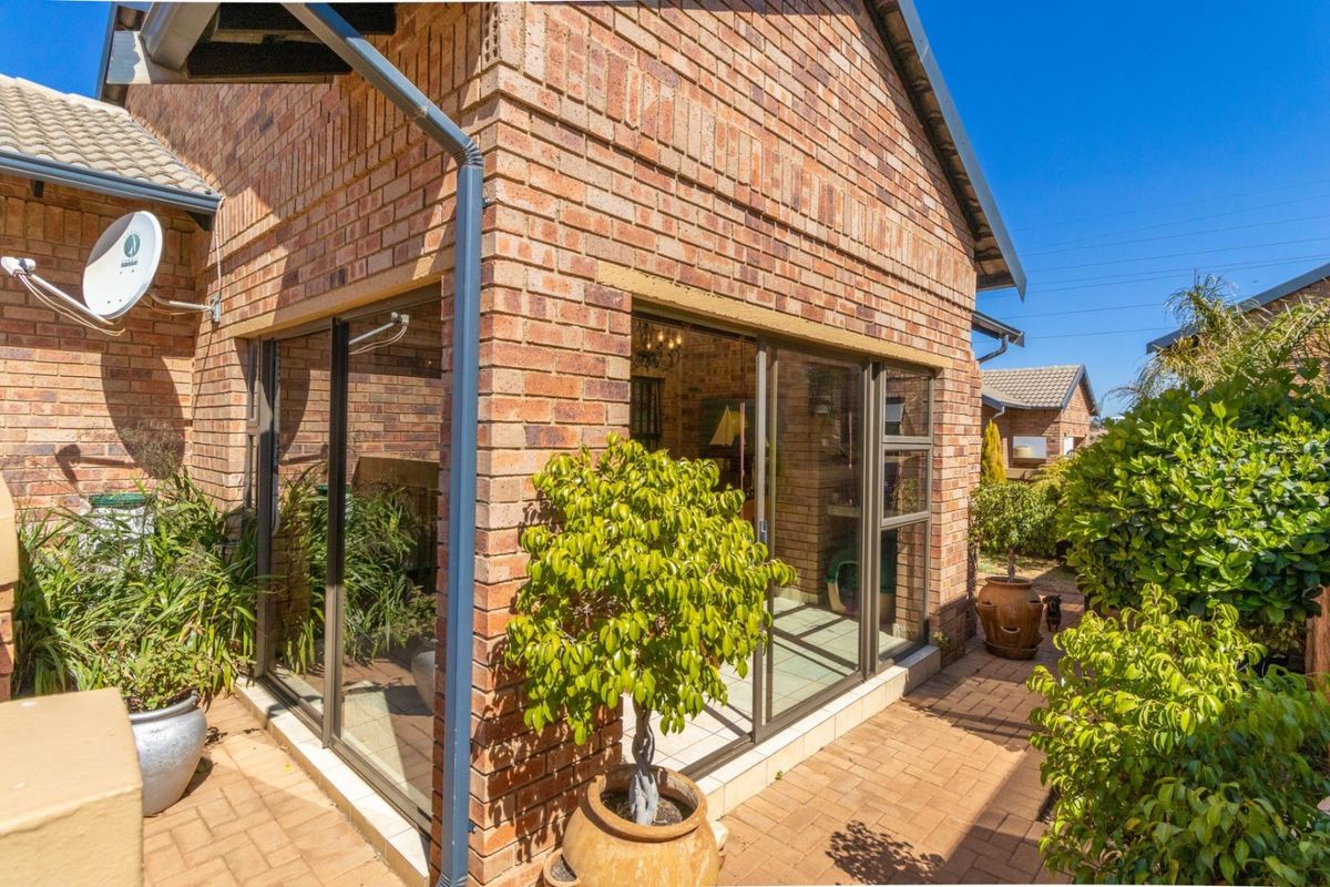 Rear exterior view of the townhouse featuring face brick construction, sliding glass doors leading to a paved patio area, and established garden surroundings.