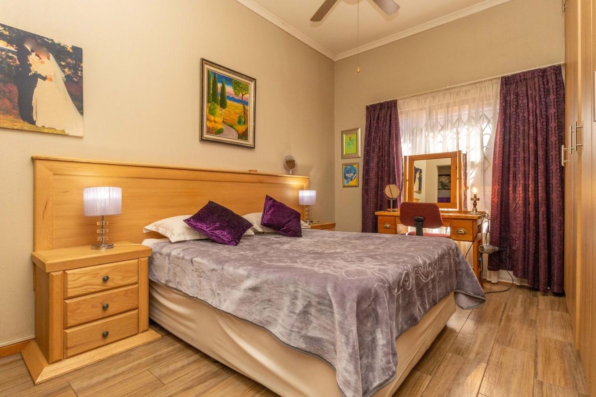 A well-maintained bedroom featuring wood-look tile flooring, a ceiling fan, and a built-in wardrobe with ample natural light.