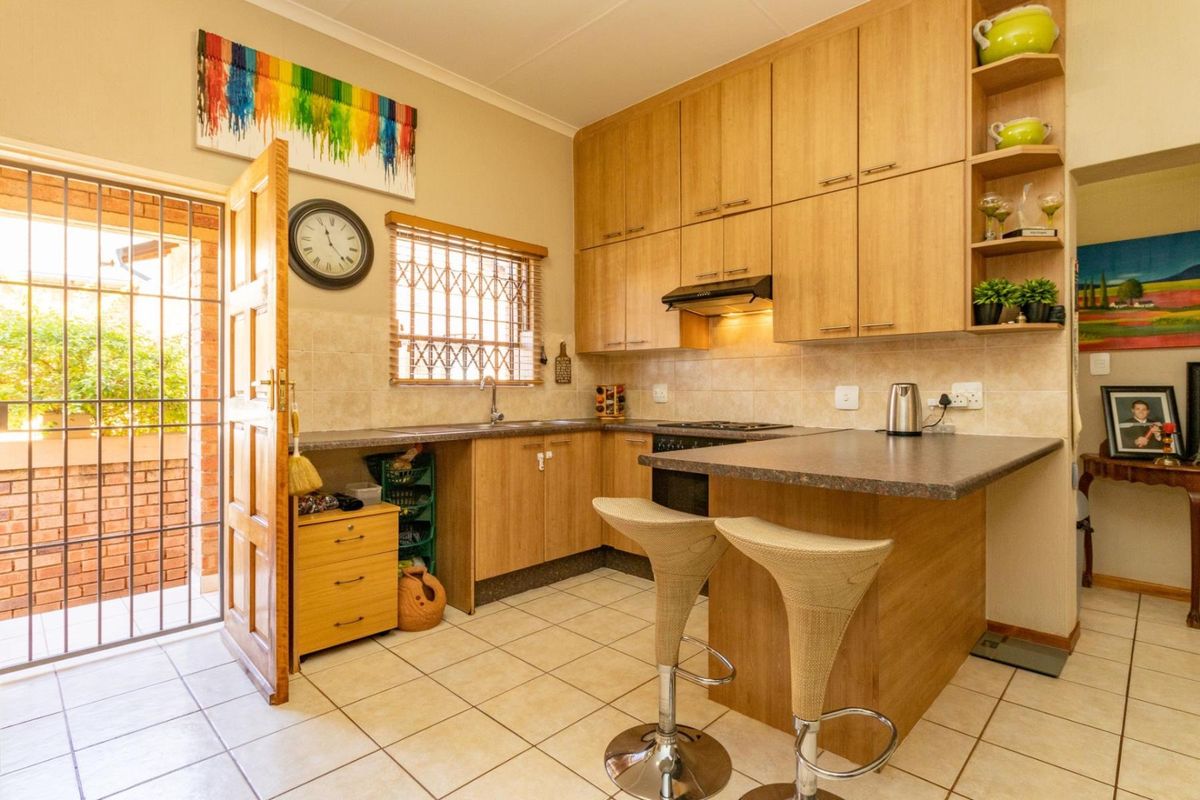 Functional kitchen featuring light wood cabinetry, laminate countertops, a breakfast nook, and tiled flooring with direct access to an exterior security gate.