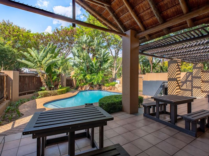 Outdoor entertainment area featuring a covered patio with a built-in braai, overlooking a private swimming pool and landscaped garden.