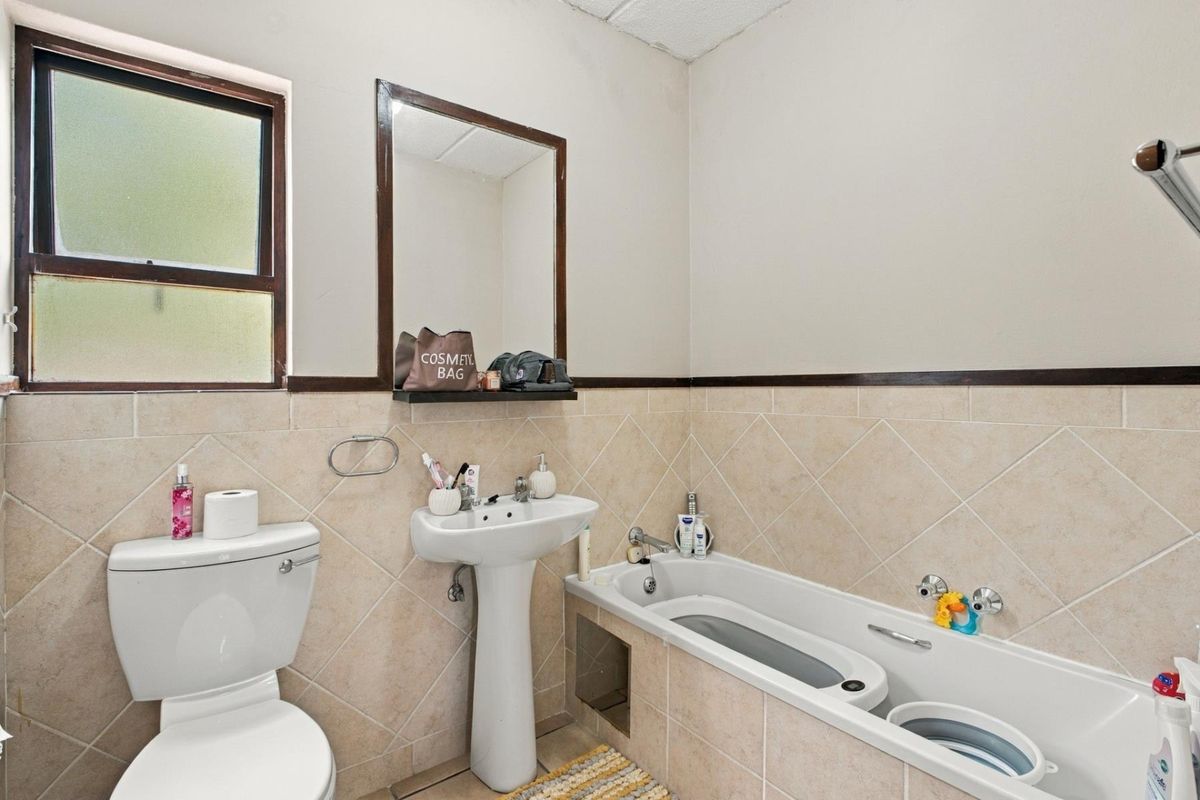 A functional bathroom featuring a pedestal basin, bathtub, and toilet with neutral wall tiling and a wall-mounted mirror.