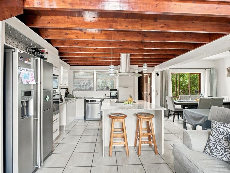 Spacious open-plan kitchen and living area featuring exposed timber ceiling beams, a central island with granite countertops, and modern tiled flooring.