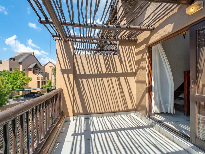 A private balcony featuring a rustic wooden pergola, tiled flooring, and a wooden balustrade, accessible via a sliding glass door.