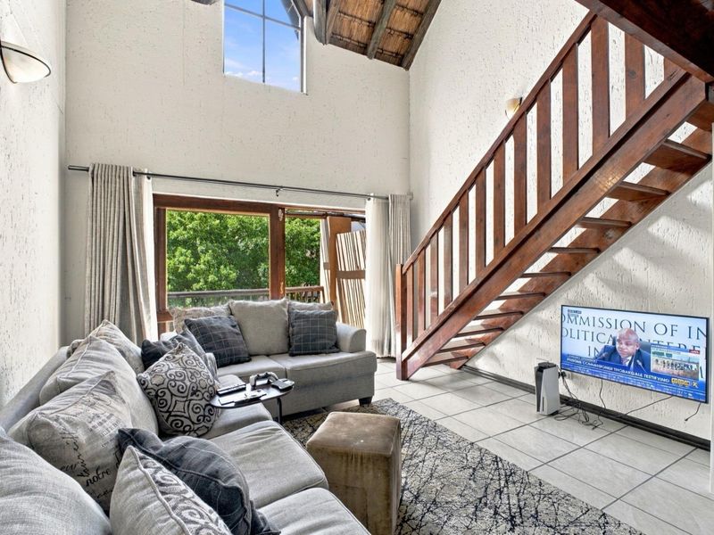 Spacious double-volume living area featuring exposed timber rafters, a wooden staircase, tiled flooring, and large windows providing natural light and garden access.