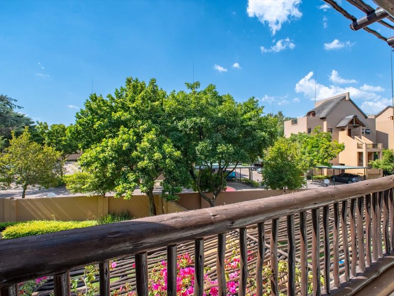 A balcony featuring a rustic wooden balustrade and pergola, offering an elevated view of the complex grounds and surrounding trees.
