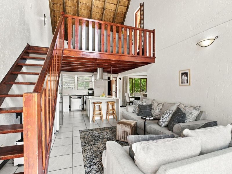 Open plan living area featuring a mezzanine level with timber staircase, thatched ceiling, and a modern kitchen island with integrated extractor fan.