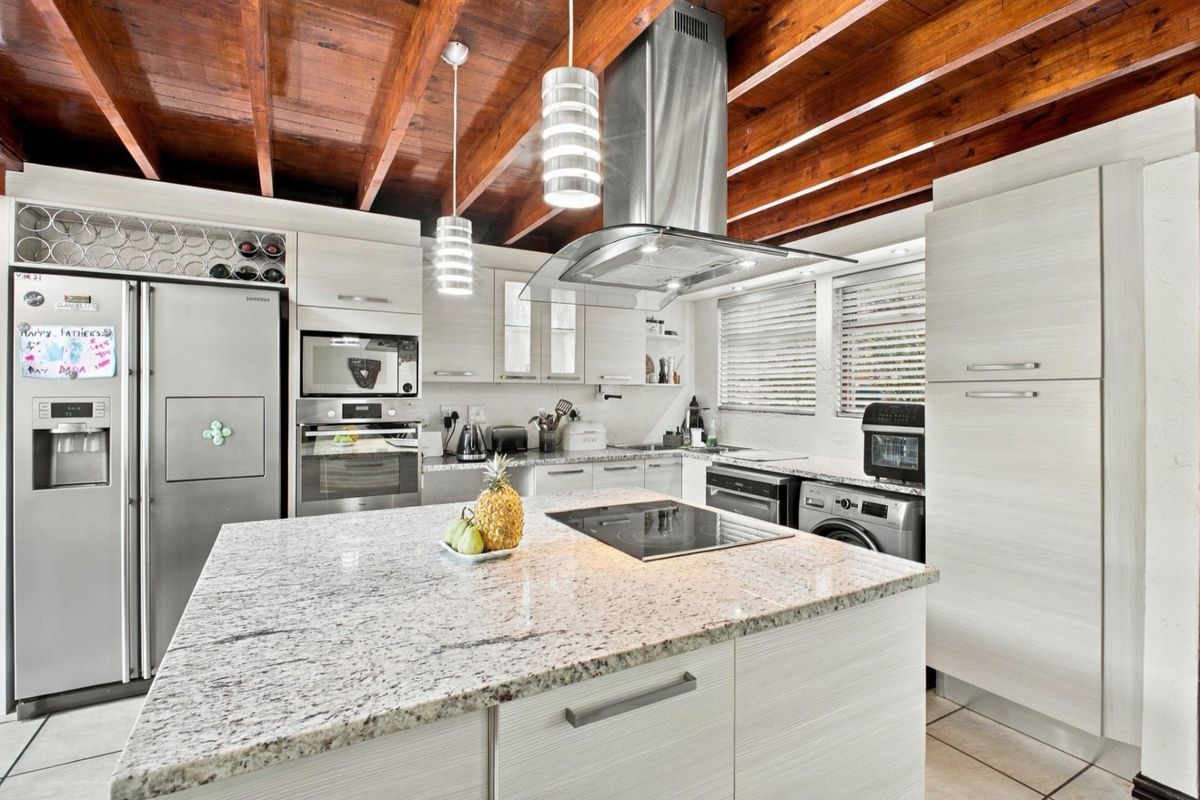 Modern kitchen featuring a granite island, built-in appliances, and distinctive exposed timber ceiling beams, offering a functional and stylish culinary space.
