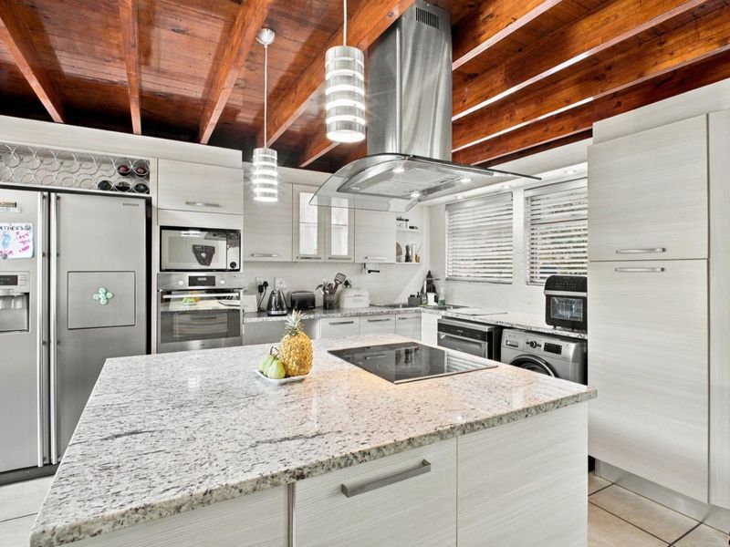 Modern kitchen featuring a granite island, built-in appliances, and distinctive exposed timber ceiling beams, offering a functional and stylish culinary space.