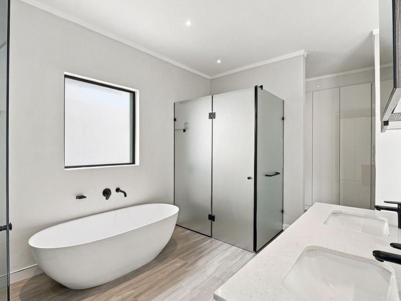 Modern bathroom featuring a sleek freestanding bathtub, a spacious walk-in shower with frosted glass, and a double vanity with contemporary black fixtures.