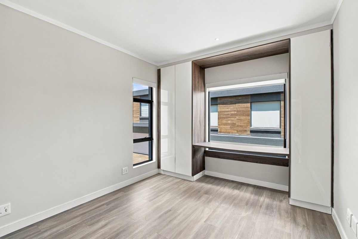 A bright, modern bedroom featuring high-quality laminate flooring, built-in cupboards, and a convenient integrated desk space.