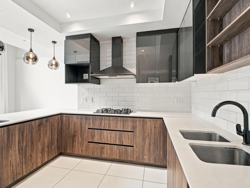 Modern kitchen featuring wood-grain cabinetry, white quartz countertops, subway tile backsplash, gas hob, extractor fan, and contemporary pendant lighting.