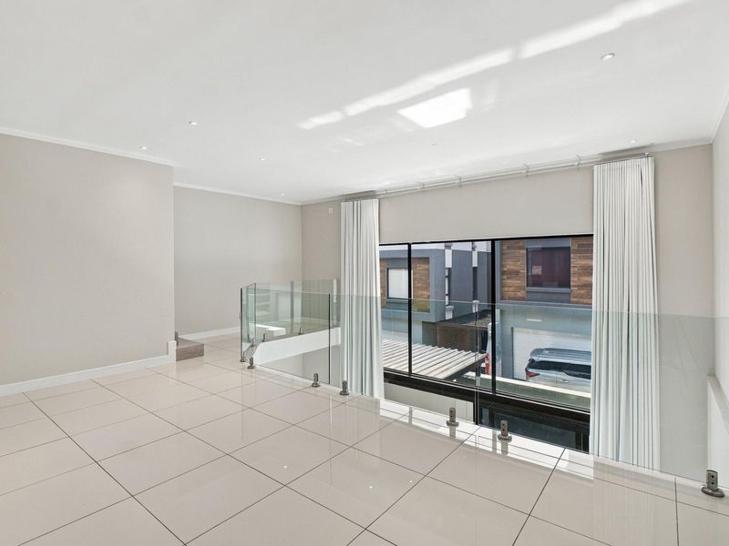 A bright and spacious open-plan living area featuring modern tiled flooring, a sleek glass balustrade, and large windows overlooking the neighborhood.