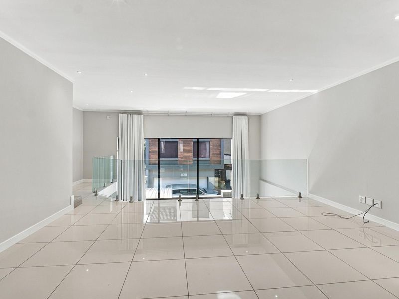 Spacious, light-filled living area featuring modern tiled flooring, recessed downlighting, and a contemporary glass balustrade overlooking the lower level.