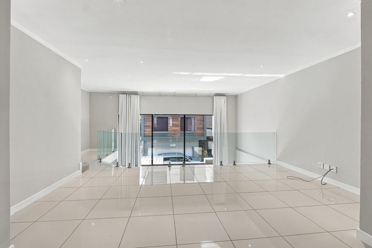 Spacious, light-filled living area featuring modern tiled flooring, recessed downlighting, and a contemporary glass balustrade overlooking the lower level.