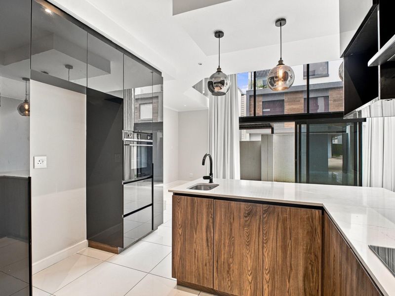 Modern kitchen featuring sleek dark cabinetry, stone countertops, built-in oven, and high-end finishes, offering a clean and contemporary culinary space.
