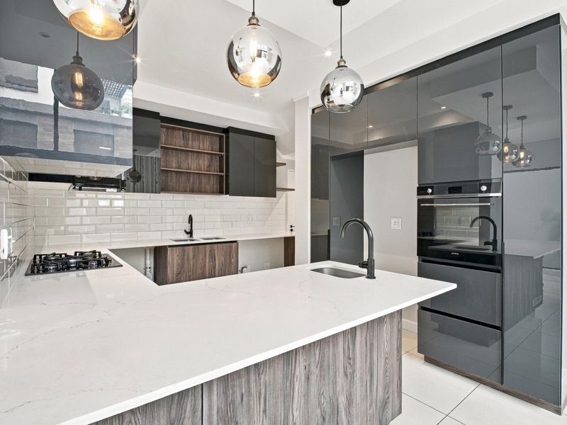 Modern kitchen featuring high-gloss cabinetry, quartz countertops, a central island with a sink, gas hob, and integrated oven, finished with stylish pendant lighting.