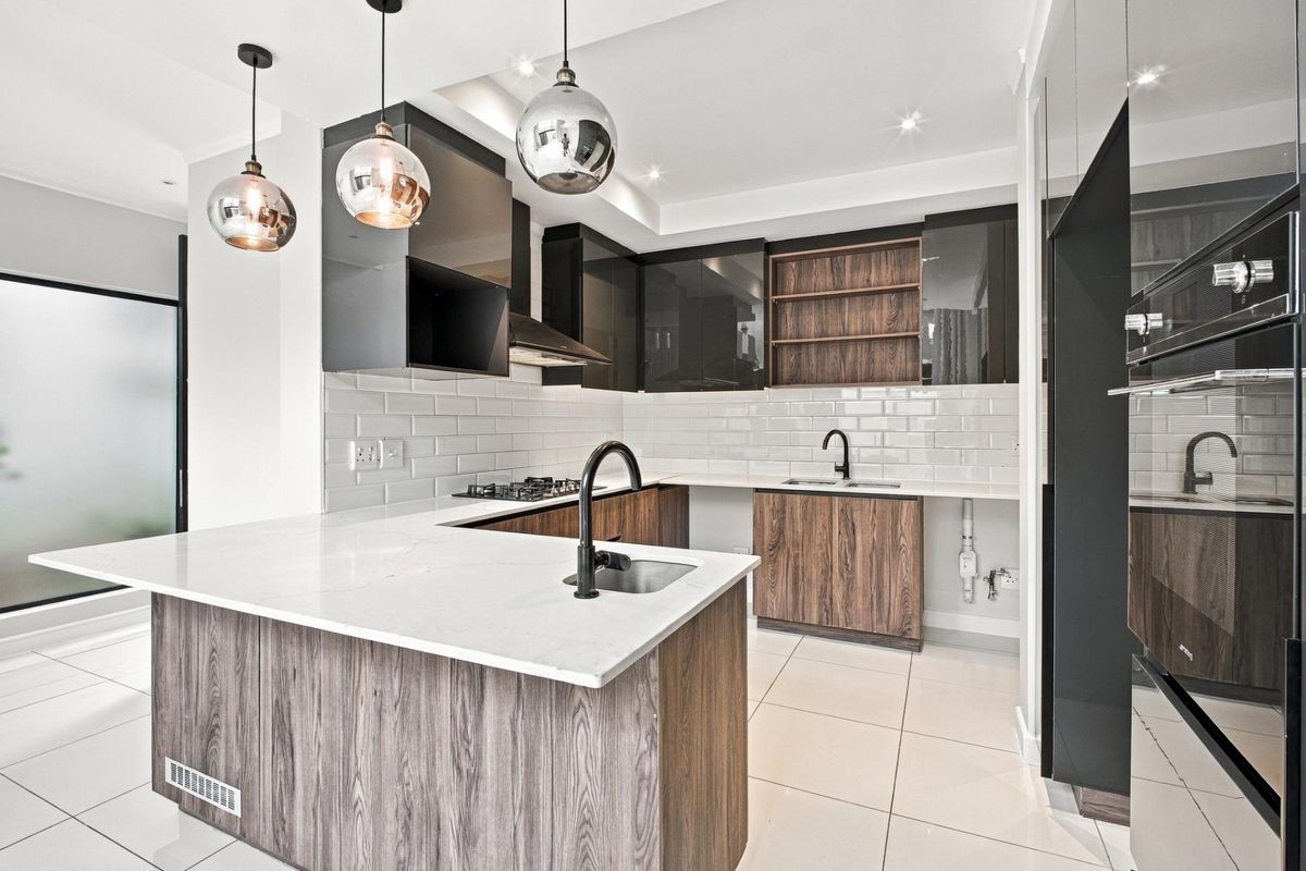 Modern kitchen featuring high-gloss and wood-grain cabinetry, quartz countertops, subway tile backsplash, and integrated appliances with contemporary pendant lighting.