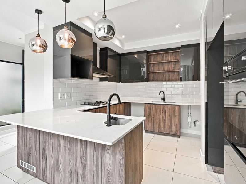 Modern kitchen featuring high-gloss and wood-grain cabinetry, quartz countertops, subway tile backsplash, and integrated appliances with contemporary pendant lighting.