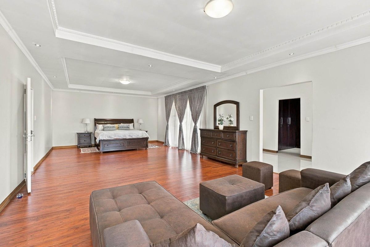 Spacious bedroom featuring warm laminate flooring, recessed ceiling lighting, decorative cove molding, and integrated built-in storage cupboards.
