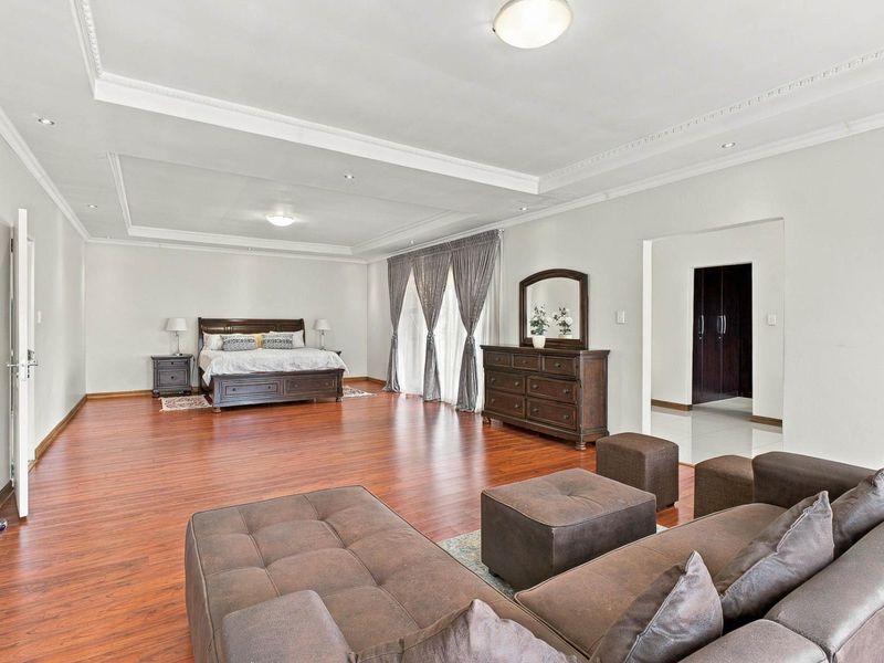 Spacious bedroom featuring warm laminate flooring, recessed ceiling lighting, decorative cove molding, and integrated built-in storage cupboards.