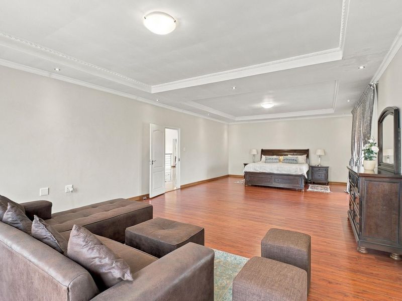 Spacious primary bedroom featuring laminate flooring, decorative cove molding, and recessed ceiling lighting, offering a generous layout with ample room for a seating area.