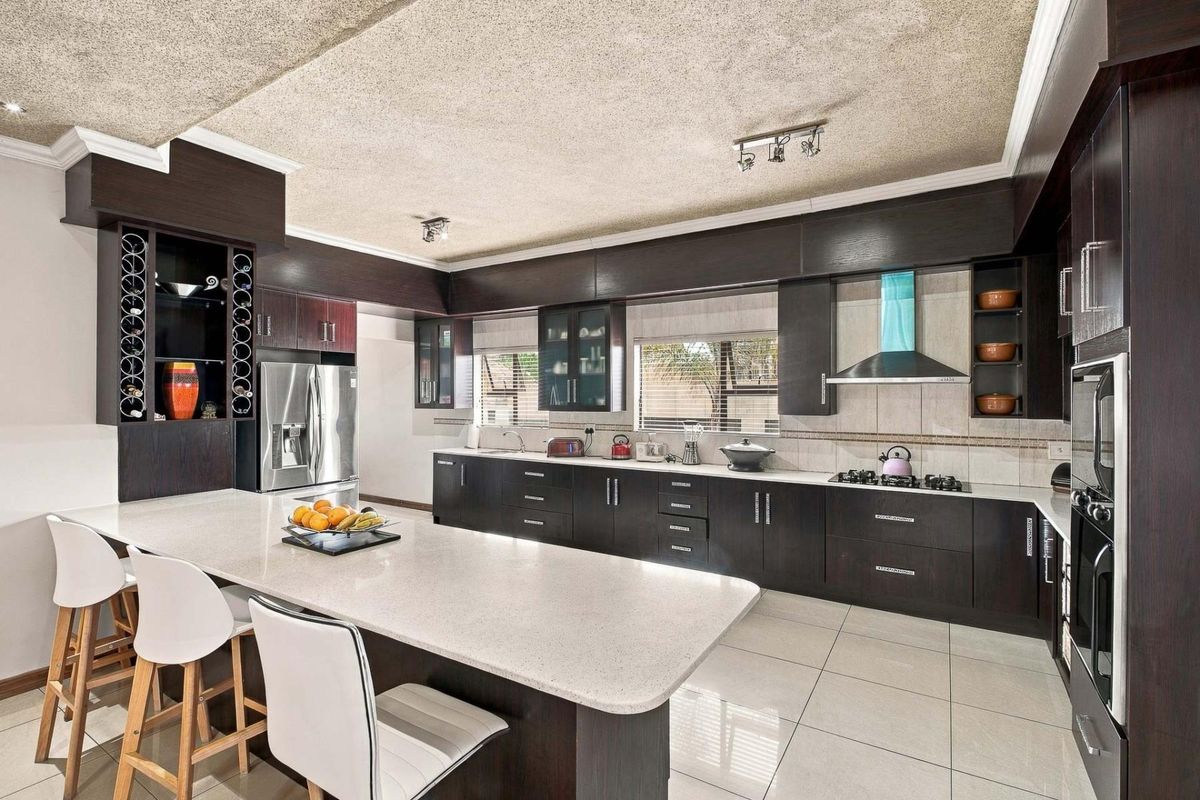Modern kitchen featuring dark wood cabinetry, stone countertops, a large central island, and integrated appliances, finished with neutral floor tiles.