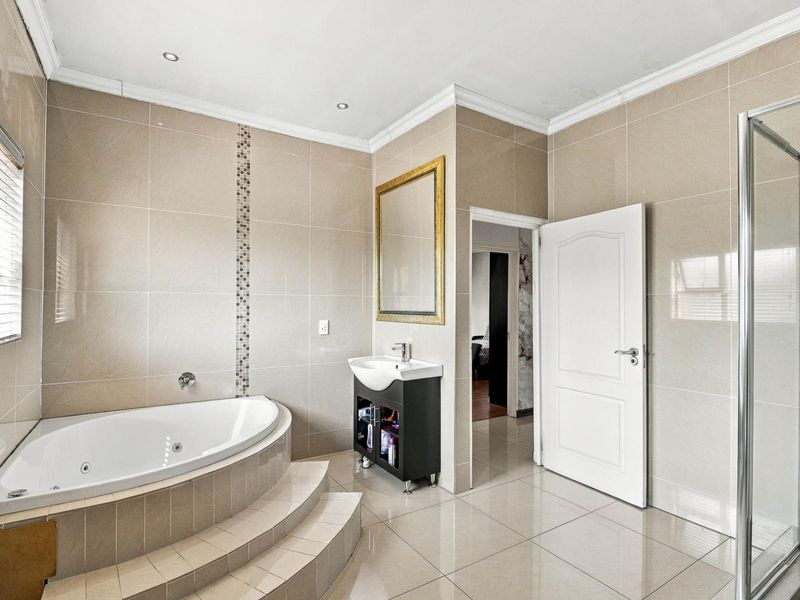 Modern bathroom featuring a corner bathtub with tiled steps, a vanity basin, and a separate shower enclosure with neutral wall and floor tiles.