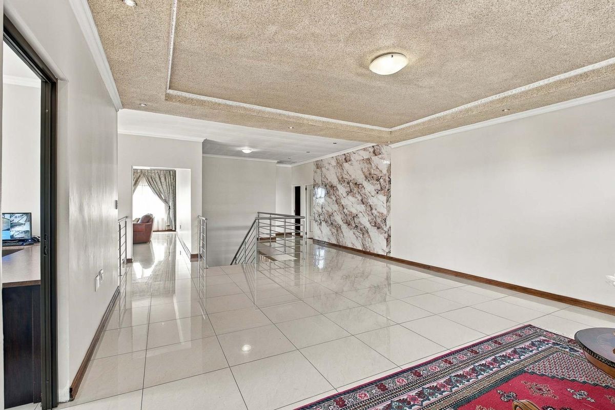 Spacious living area featuring polished porcelain floor tiles, a decorative textured ceiling, and a striking marble-effect feature wall with modern staircase railing.