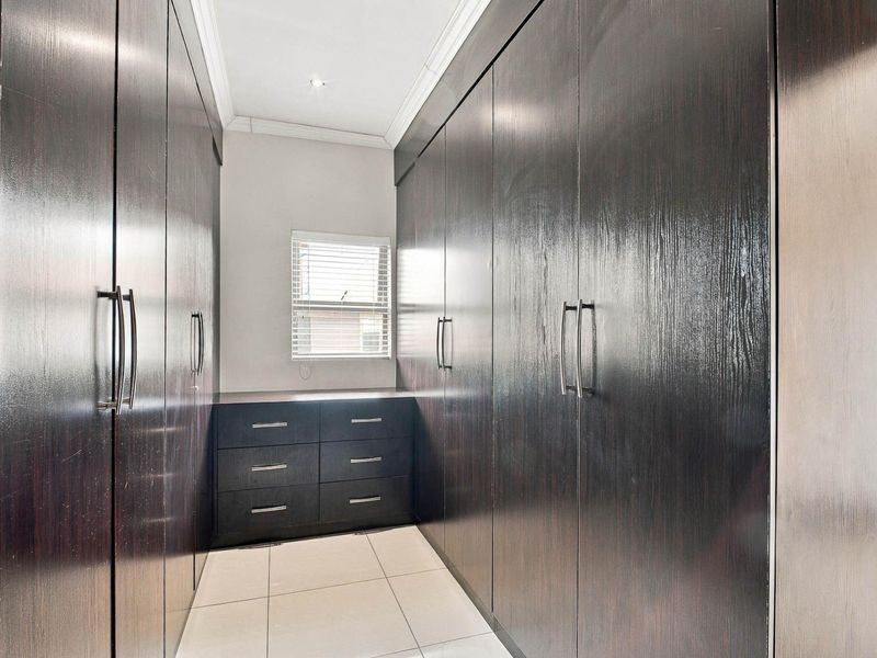 A walk-in dressing room featuring extensive dark wood built-in cabinetry, tiled flooring, and a window with venetian blinds.
