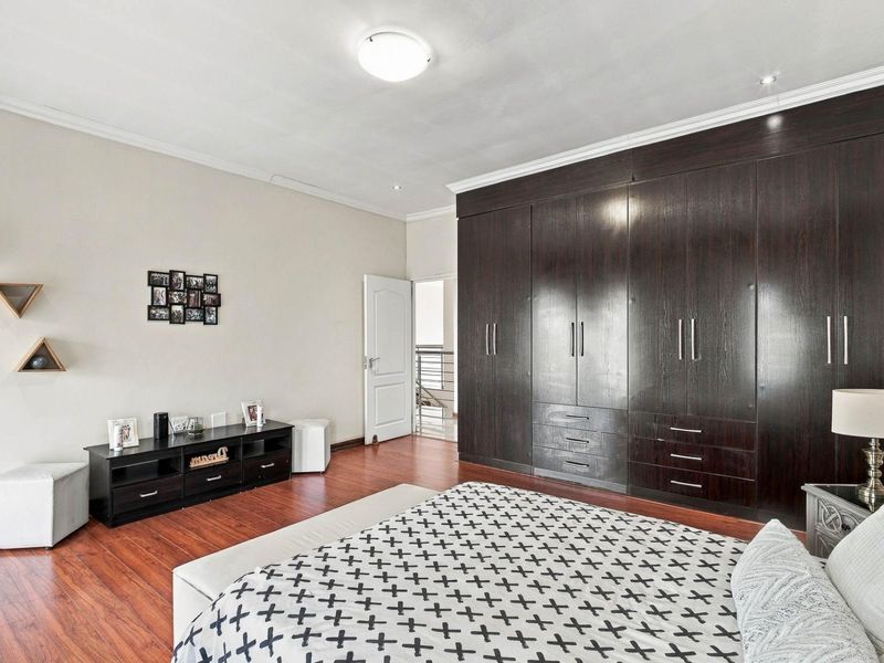 Spacious bedroom featuring dark wood built-in cupboards, warm laminate flooring, and clean finishes, offering ample storage and a comfortable living environment.