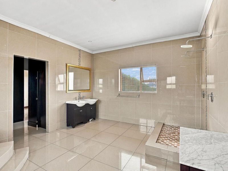 Spacious modern bathroom featuring a double vanity, large walk-in shower with mosaic tile accents, and neutral floor-to-ceiling wall tiles.