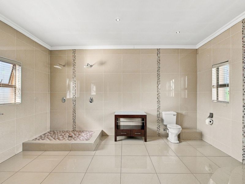 Spacious bathroom featuring a walk-in shower with dual shower heads, a vanity cabinet, and a toilet, finished with neutral floor-to-ceiling tiling.