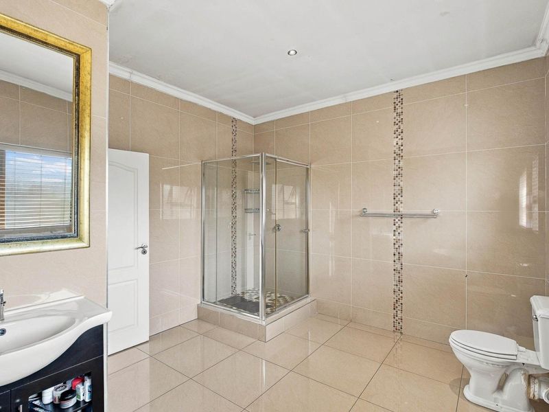 A spacious, fully tiled bathroom featuring a glass shower enclosure, vanity basin, and toilet, finished with neutral wall and floor tiles.