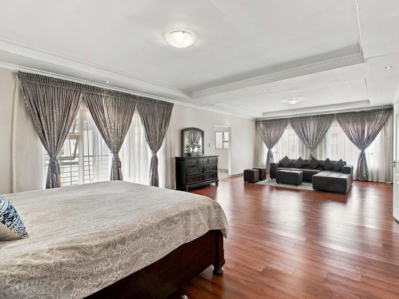Spacious master bedroom featuring rich hardwood flooring, elegant crown molding, recessed lighting, and large windows with ample natural light.