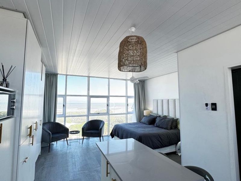 Modern open-plan studio apartment featuring a sleek kitchen island, contemporary cabinetry, and expansive floor-to-ceiling windows offering panoramic coastal views.