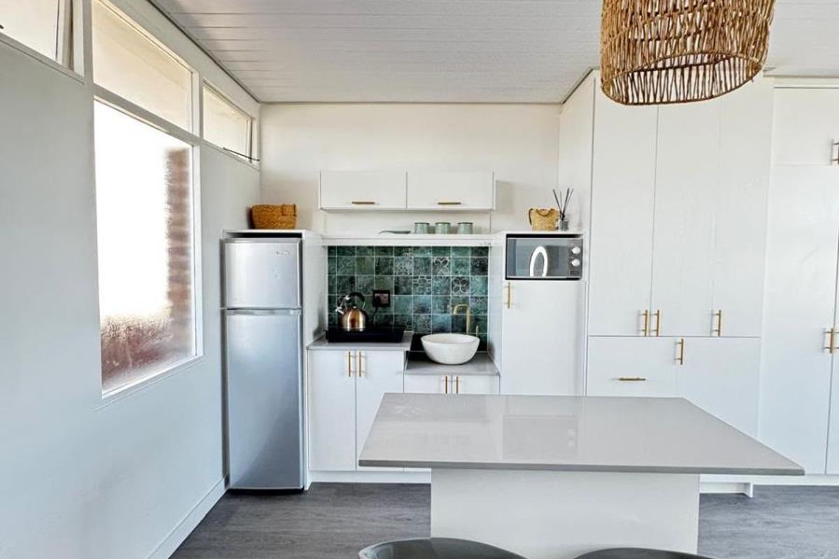 Modern kitchen featuring white cabinetry, stone countertops, a decorative tiled backsplash, and a central island with integrated storage and seating.