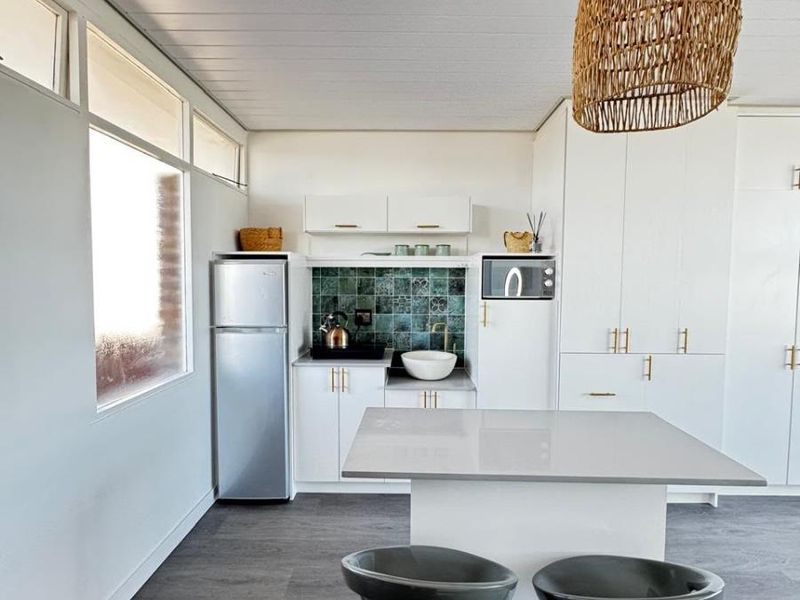 Modern kitchen featuring white cabinetry, stone countertops, a decorative tiled backsplash, and a central island with integrated storage and seating.