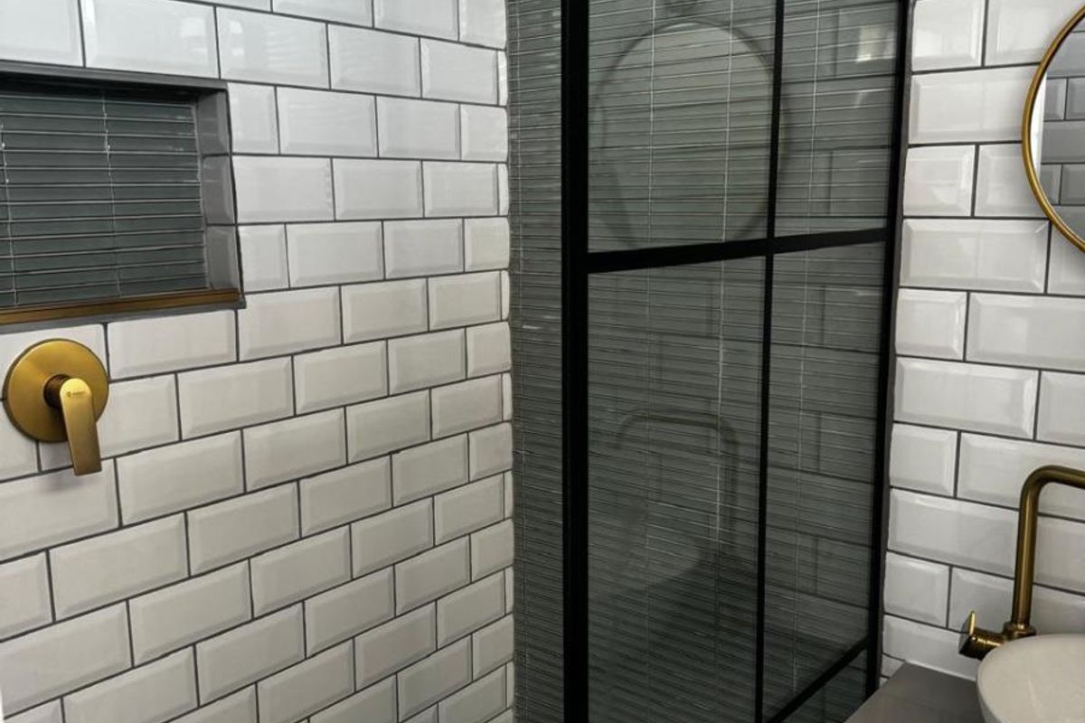 Modern bathroom featuring a walk-in shower with black-framed glass screen, brass fixtures, subway tiling, and a sleek vanity with a vessel sink.