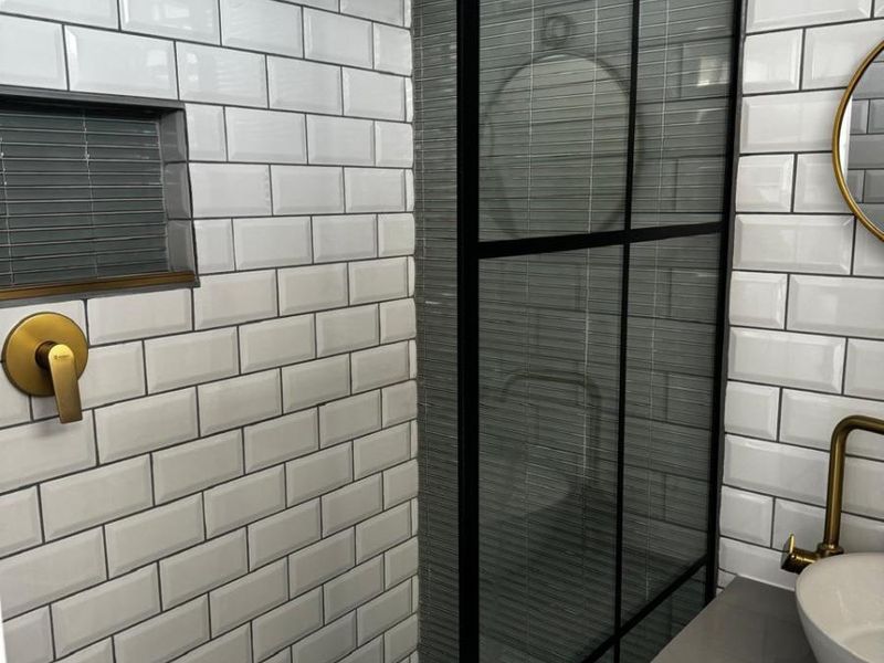 Modern bathroom featuring a walk-in shower with black-framed glass screen, brass fixtures, subway tiling, and a sleek vanity with a vessel sink.