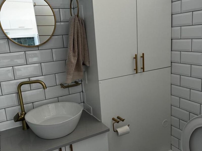 Modern bathroom featuring white subway tile walls, a vessel sink with brass fixtures, and ample built-in storage cabinetry.