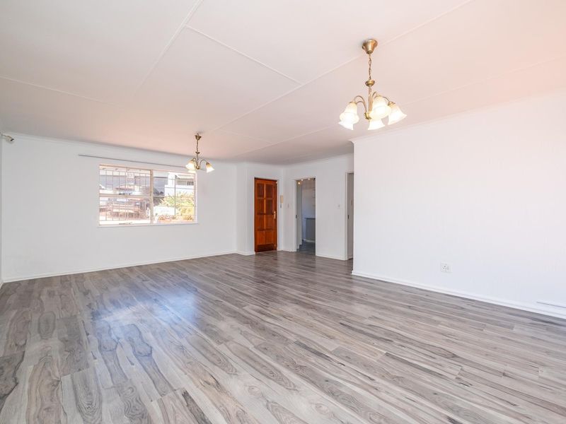 A spacious, empty living area featuring modern grey laminate flooring, neutral white walls, and classic ceiling light fixtures.