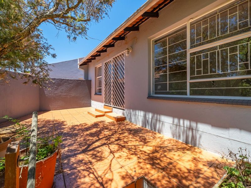 A rear exterior view of the townhouse featuring a tiled patio area, security gates, and perimeter boundary walls.