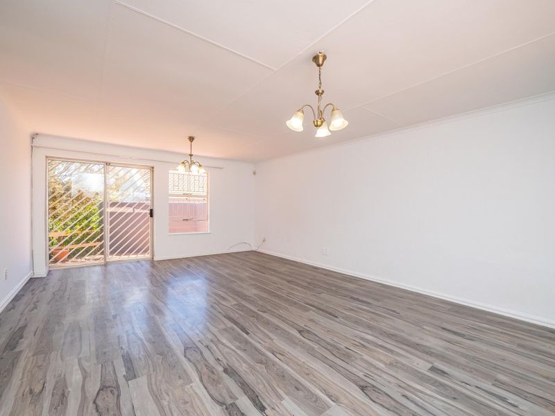 Spacious, empty living area featuring modern grey laminate flooring, neutral walls, and a sliding glass door providing access to the exterior.