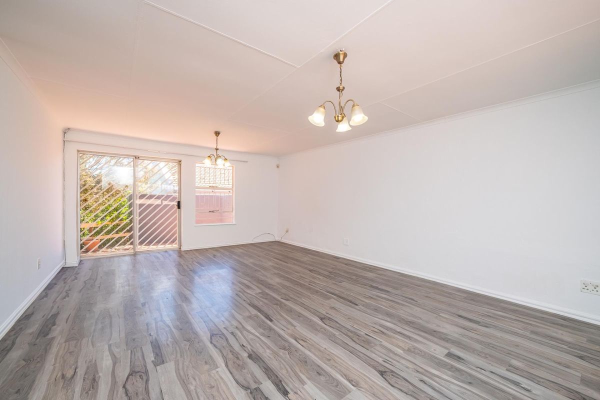Spacious, empty living area featuring modern grey laminate flooring, neutral walls, and a sliding glass door providing access to the exterior.