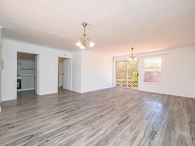 Spacious, light-filled living area featuring modern laminate flooring, neutral walls, and direct access to an outdoor space through a sliding glass door.