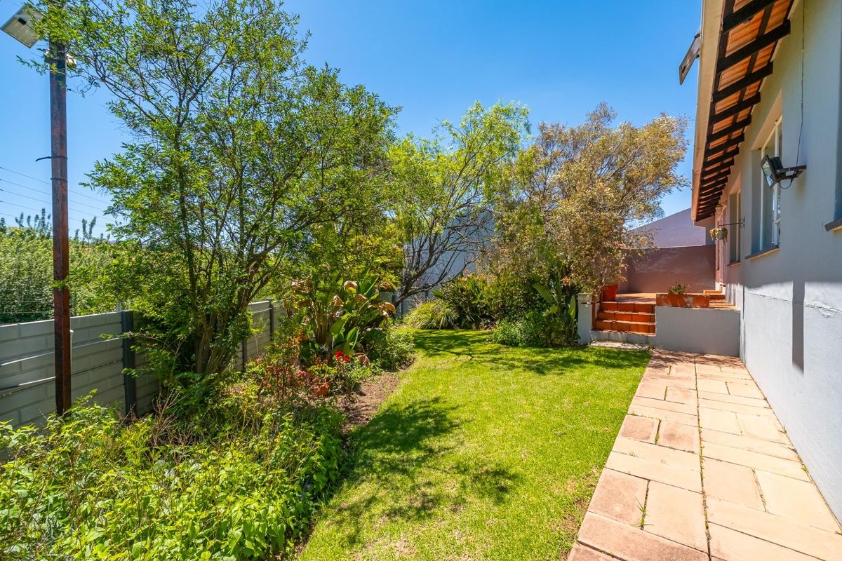 A private rear garden featuring a paved walkway, established greenery, and a raised patio area accessible from the townhouse.