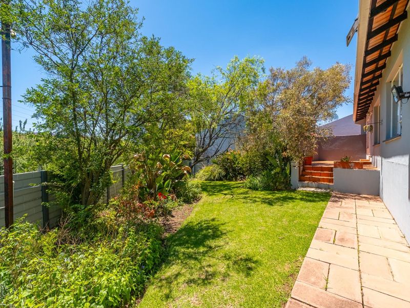 A private rear garden featuring a paved walkway, established greenery, and a raised patio area accessible from the townhouse.